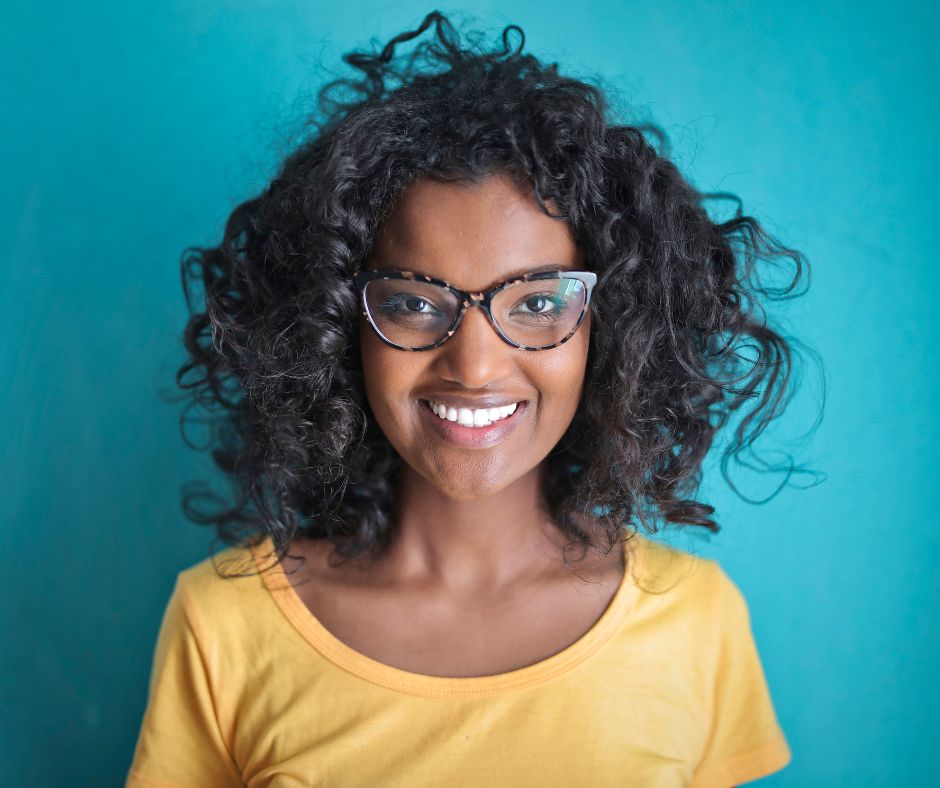 mulher jovem de pele negra sorrindo e com óculos de grau