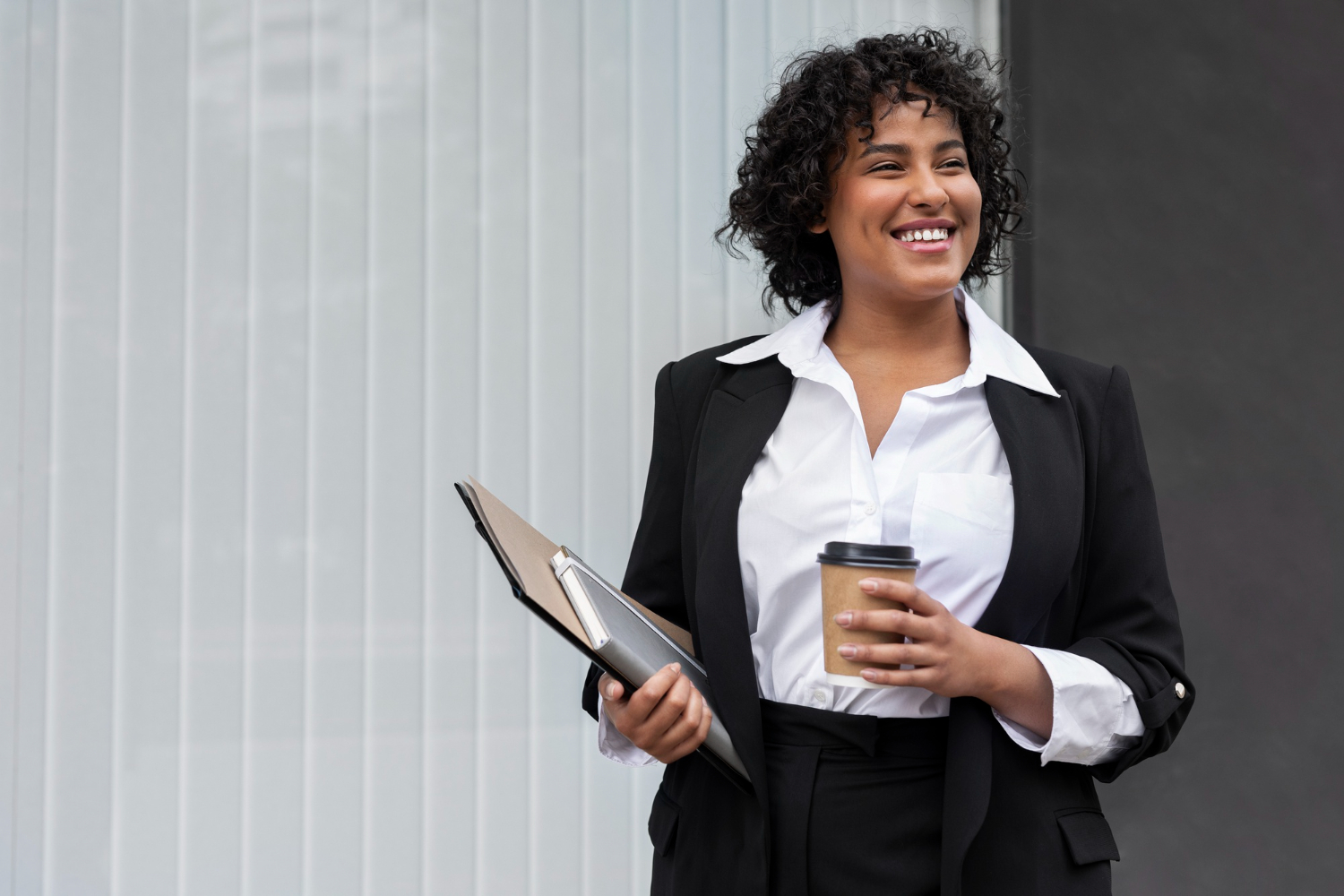 Mulher negra sorrindo segurando um café e uma prancheta