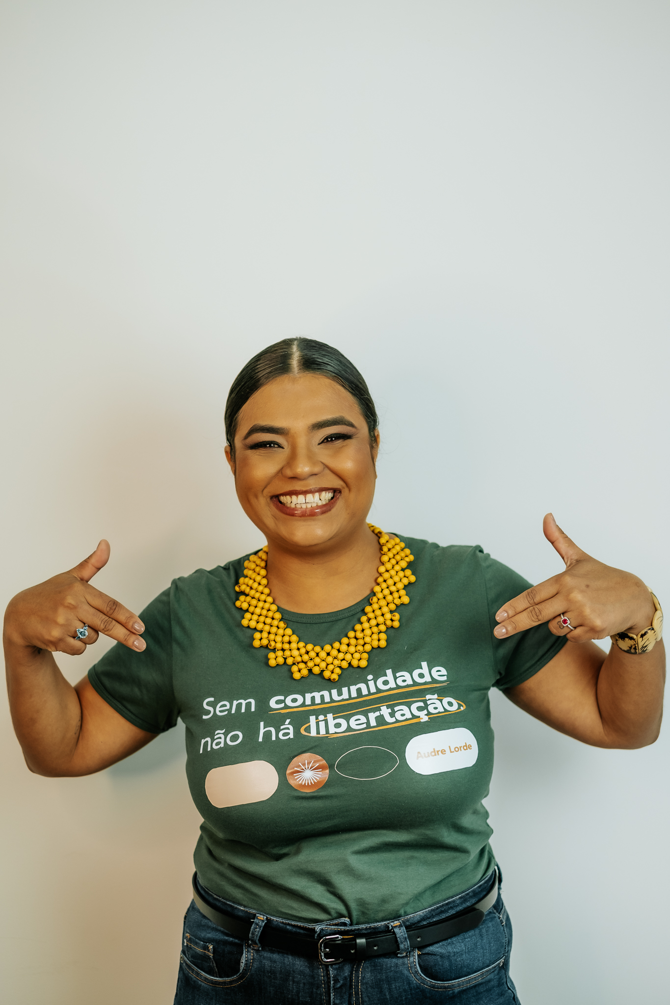 Mulher negra feliz com os dedos apontados para a frase da sua camisa