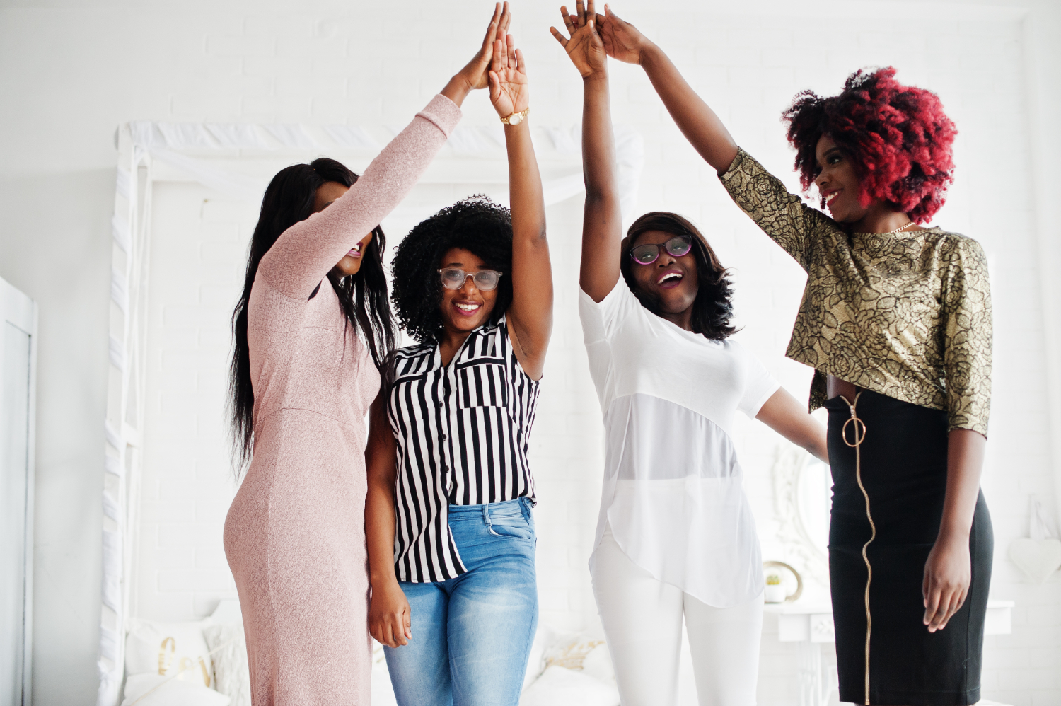 Quatro mulheres celebrando juntas em um ambiente claro e acolhedor. Elas estão com os braços levantados, unindo as mãos no alto, simbolizando união e conquistas. A diversidade de estilos e expressões transmite energia positiva e determinação, representando um momento de celebração coletiva. Essa imagem pode ilustrar o conceito de uma jornada 2024 repleta de desafios superados e metas alcançadas, com foco na colaboração e no empoderamento.