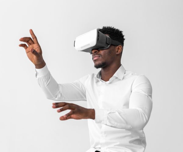 homem negro vestido de camisa branca, usando um óculos de realidade virtual e fazendo movimento com as mãos