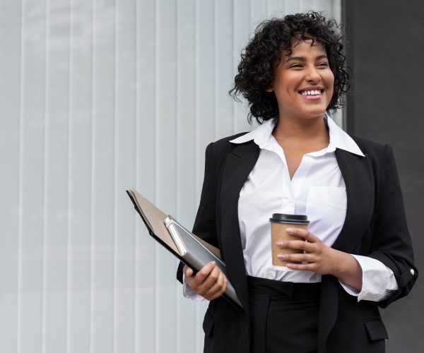 Mulher negra sorrindo segurando um café e uma prancheta