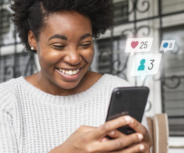 mulher negra olhando para o celular e sorrindo para exemplificar alguém que está olhando para estratégia de tráfego e vendas do seu negócio.