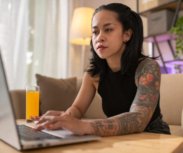 Uma mulher de origem indígena, concentrada trabalha em um laptop em um ambiente acolhedor, com uma luminária acesa ao fundo e um copo de suco na mesa. A cena reflete a criatividade e o foco necessários no desenvolvimento de estratégias de branding digital, destacando o uso de ferramentas online para fortalecer a identidade de marcas no ambiente virtual.