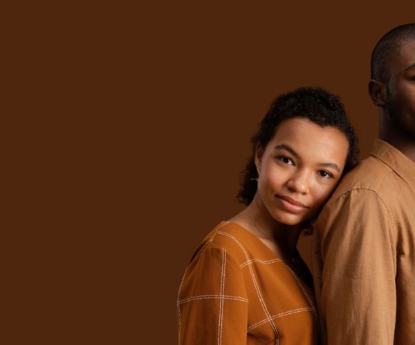 pessoas negras: um homem negro alto vestido de camiseta bege e uma mulher negra um pouco mais baixa que o homem e vestida de camisa marrom, encosta a cabeça em suas costas
